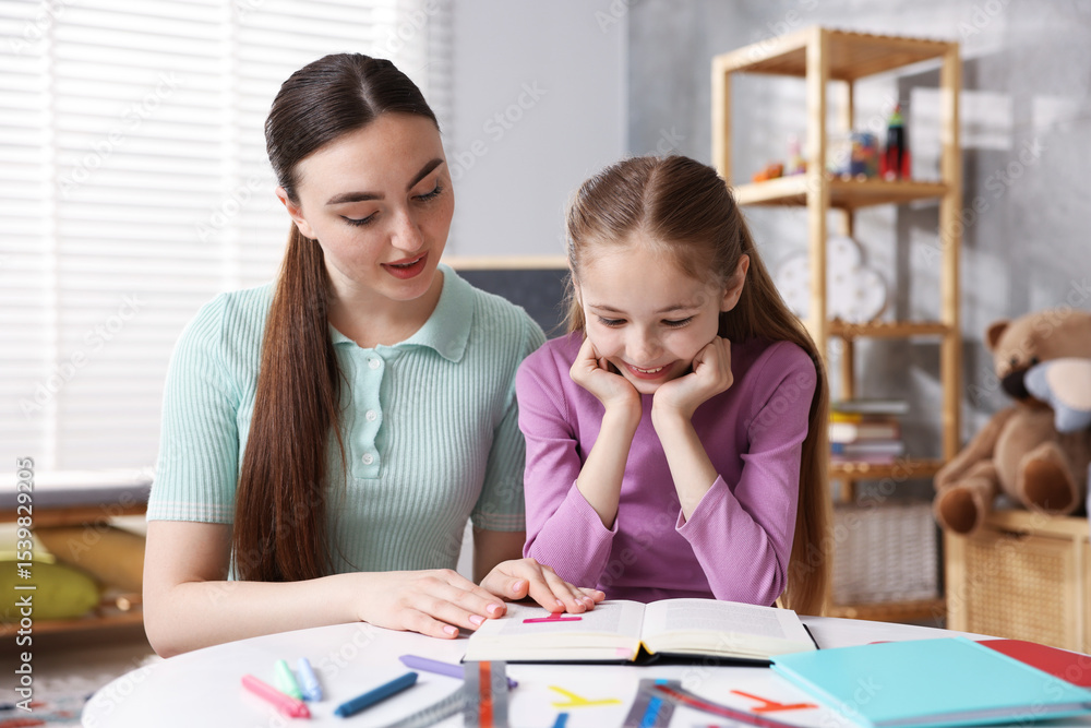 Dyslexia. Mother and her daughter reading book at table indoors Dyslexia. Mother and her daughter reading book at table indoors