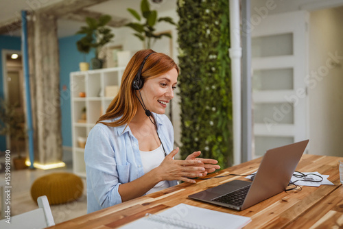 Fotografija red head woman operator with headset talk on video call with client