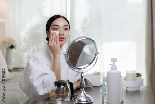 Murais de parede Young asian woman removing makeup with cotton pad in front of mirror