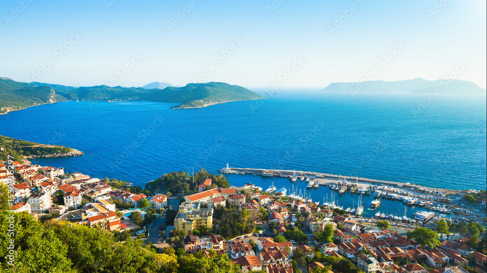 Aerial panoramic morning view of Kas, picturesque coastal town in Turkey along Mediterranean Sea. Scenic landscape shows Kas with its marina, surrounding bay, and distant islands under clear sky Aerial panoramic morning view of Kas, picturesque coastal town in Turkey along Mediterranean Sea. Scenic landscape shows Kas with its marina, surrounding bay, and distant islands under clear sky