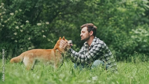 young man in plaid shirt playing training petting hugging and kissing his dog during summer park walk happy loving companionship concept lifestyle

