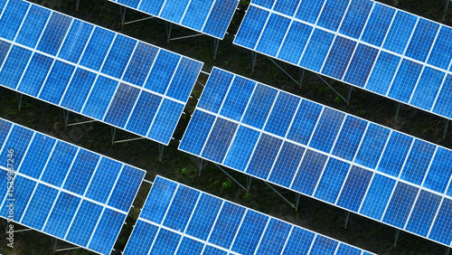 Overhead shot of a solar farm with multiple aligned blue solar panels absorbing sunlight, representing innovative green technology and efforts toward reducing carbon footprint.
