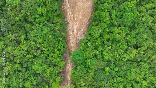 Drone aerial view of a landslide cutting through forest, illustrating how climate change intensifies rainfall patterns, leading to increased soil erosion and ecosystem disruption. Thailand.
