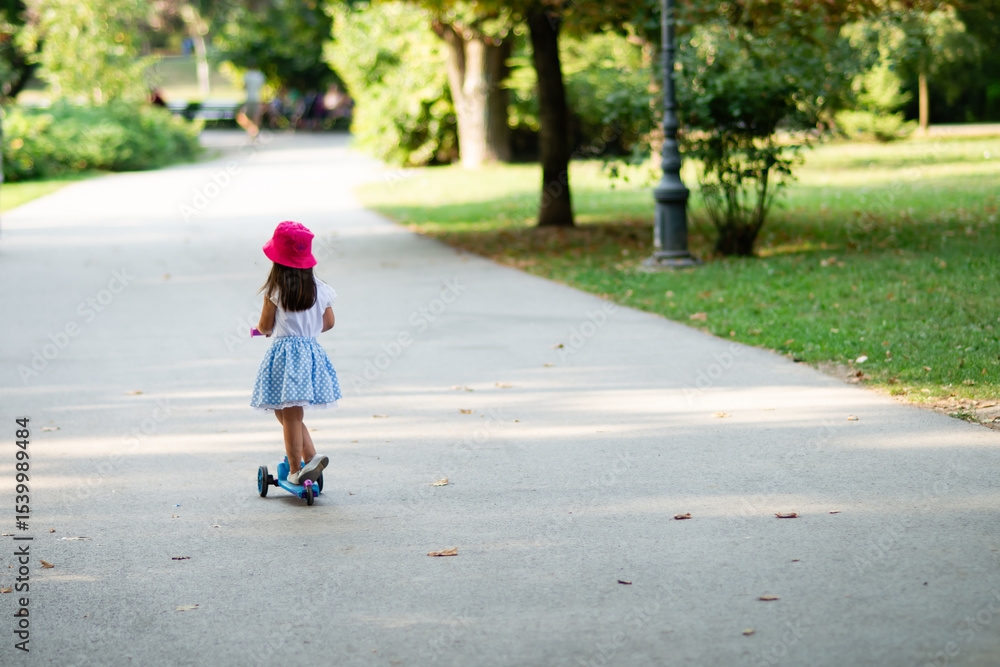 Fototapeta premium Little girl riding scooter in park during summertime