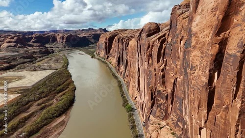 Potash Road in Moab, Utah. Close up of High Rising Red Cliffs on side of highway. Colorado River, Partly Cloudy Sky