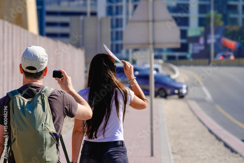 Due giovani, uno con zaino e videocamera e l'altra con lunghi capelli neri, camminano su un marciapiede urbano sotto il sole. Questa immagine cattura l'essenza dell'esplorazione cittadina e della crea