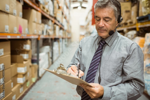 Tableau sur toile Senior male supervisor in suit with clipboard checking boxes on warehouse racks,