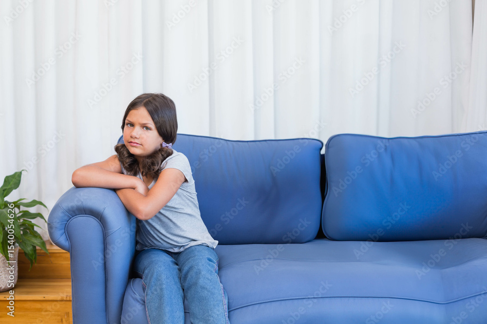 Female child sitting on blue couch in living room with potted plant, white curtains, copy space Female child sitting on blue couch in living room with potted plant, white curtains, copy space
