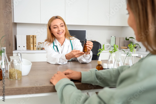 Female homeopathic doctor with dropper bottle and patient at table in office