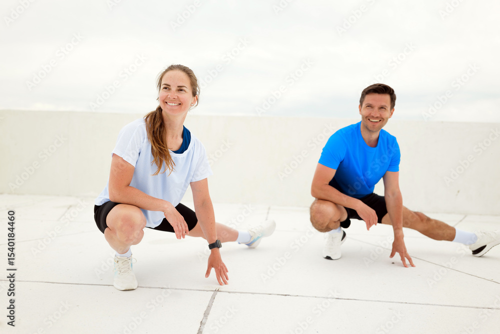 Obraz premium Fitness Enthusiasts Enjoy Dynamic Stretching on a Rooftop While Preparing for Their Workout, Embracing the Fresh Air and Open Space