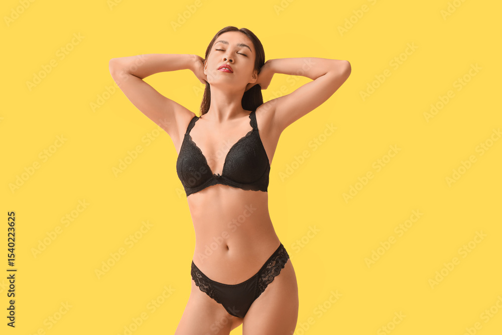 Naklejka premium Beautiful young Asian woman in sexy black underwear on yellow background