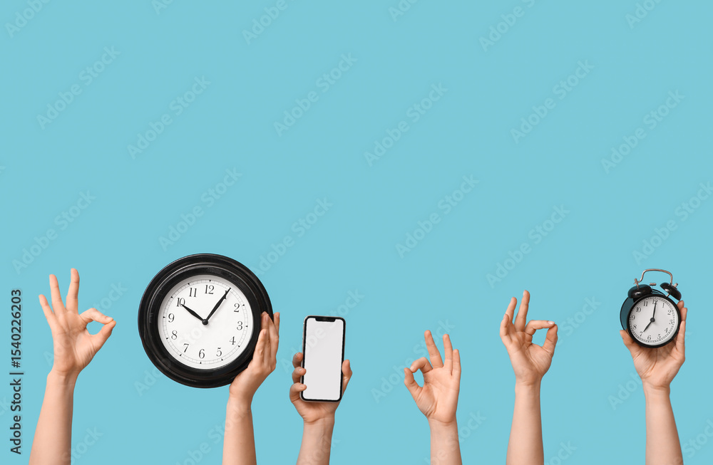 Obraz premium Female hands with clocks and blank mobile phone showing OK on blue background