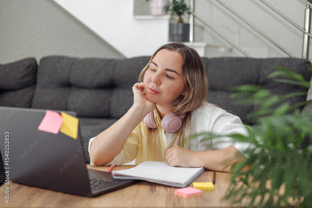 Young blond European woman with headphones lying on floor near laptop and notebook in modern living room Young blond European woman with headphones lying on floor near laptop and notebook in modern living room