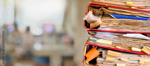 stack of messy file folders with narrow depth of field, blurred office in the back,beat the clock,stress,red tape, bureaucracy, heavy workload,business concept. 