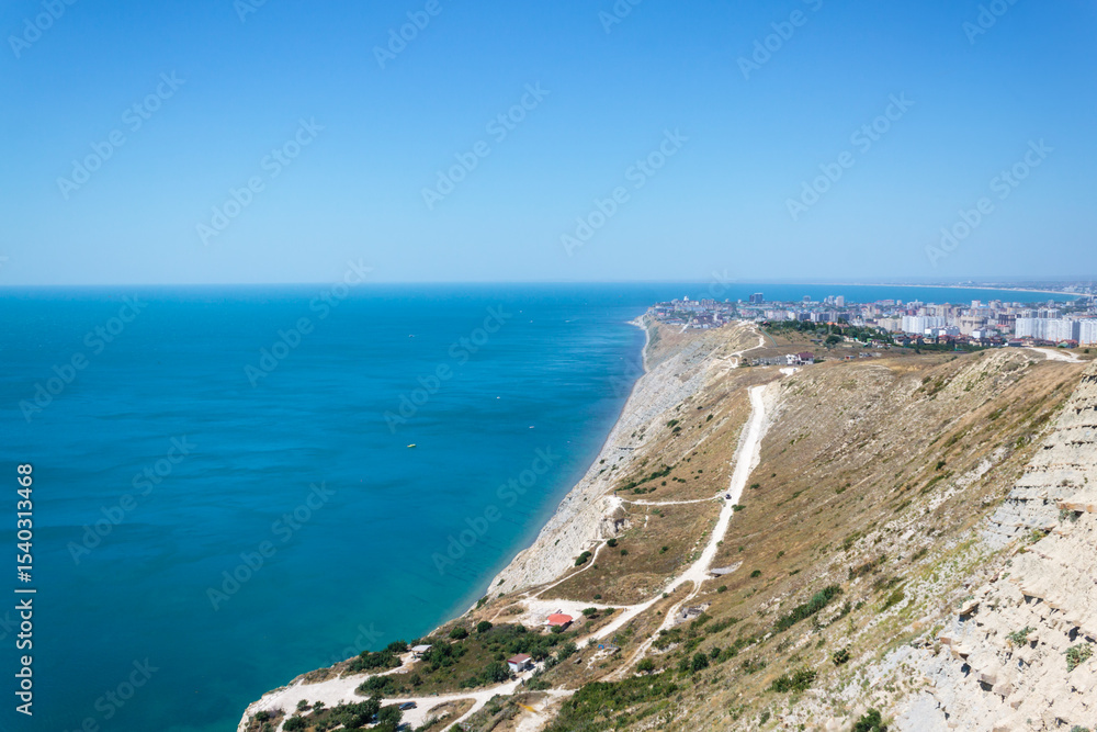 Obraz premium A stunning panoramic view of the seascape of the Black Sea, the Anapa Bay, the foot of the Caucasus Mountains and the tourist city of Anapa from a steep rocky cliff of a white limestone bald mountain.