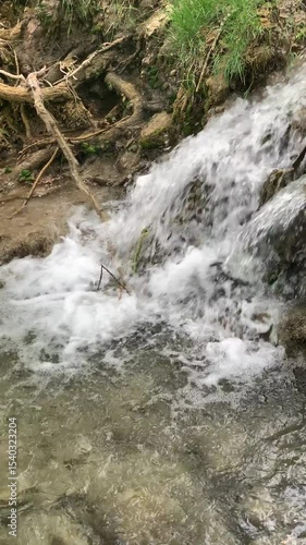 A stream of water is flowing down a rocky hillside. The water is clear and calm, and the rocks are scattered throughout the area. The scene is peaceful and serene, with the sound of the water