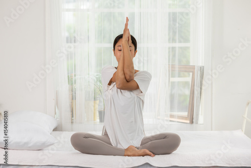 Wallpaper Mural Asian woman practicing yoga meditation indoors, sitting cross legged on bed, performing eagle pose, calm and peaceful atmosphere with natural lighting Torontodigital.ca