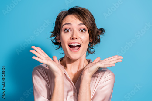 Schilderij op canvas Joyful young woman in satin blouse expressing happiness against a vibrant blue b