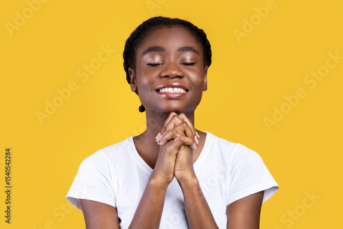 Fotografia African American Woman Praying Holding Hands In Prayer Gesture Standing On Yellow Studio Background, Smiling With Eyes Closed