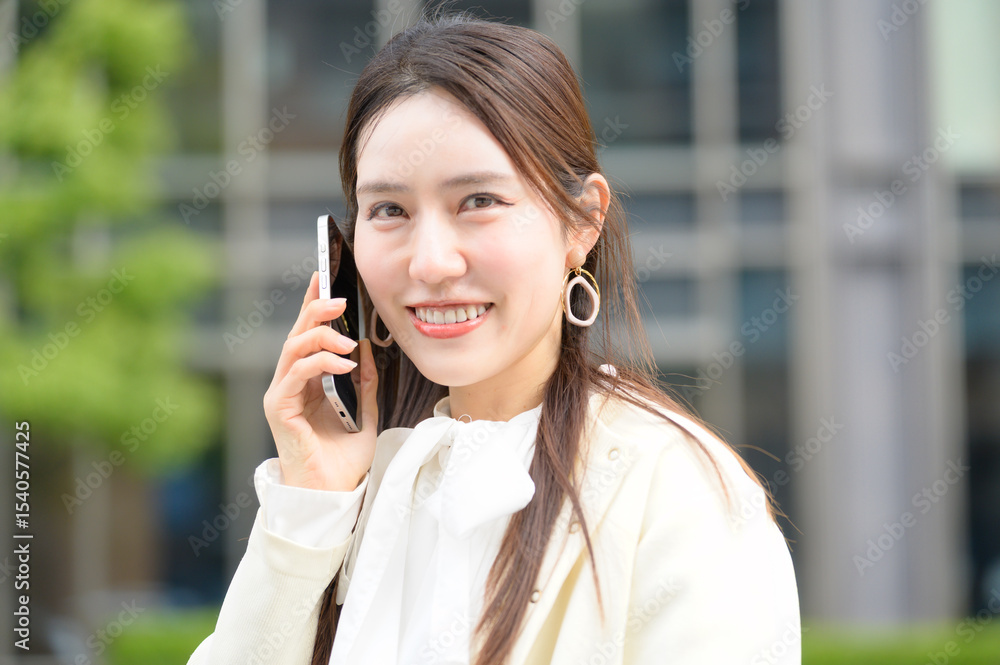 街中でスマートフォン通話をしながら微笑む白い服の女性のポートレート 街中でスマートフォン通話をしながら微笑む白い服の女性のポートレート