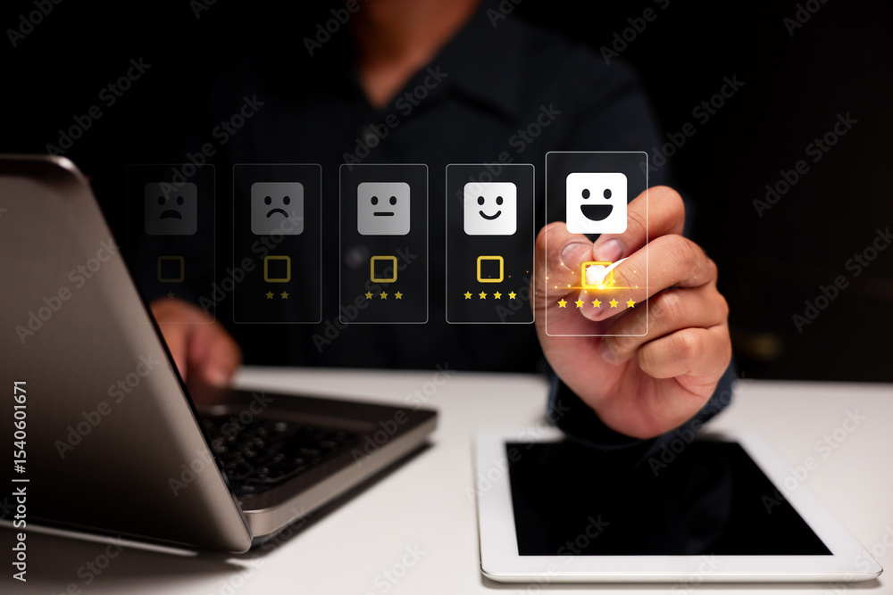 A person selects a five-star happy face rating on a digital screen, with a laptop and tablet in the background, symbolizing user feedback or customer satisfaction. A person selects a five-star happy face rating on a digital screen, with a laptop and tablet in the background, symbolizing user feedback or customer satisfaction.