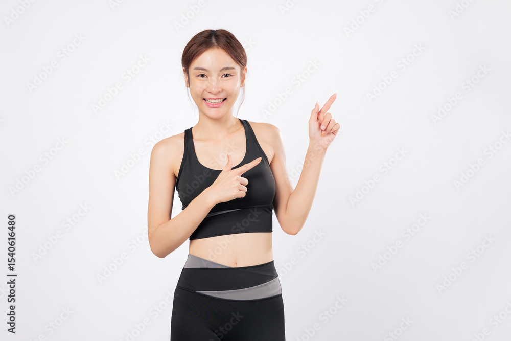 Point to the sky with a confident smile fit woman shows her points again, standing strong in black sportswear and embracing her fitness journey with grace and energy. isolated studio white background Point to the sky with a confident smile fit woman shows her points again, standing strong in black sportswear and embracing her fitness journey with grace and energy. isolated studio white background