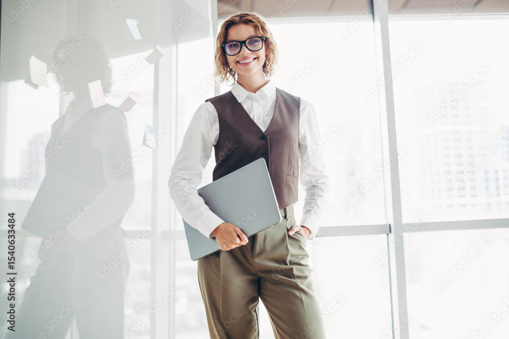 Fototapeta premium Confident businesswoman in stylish formalwear holding a laptop in an office environment