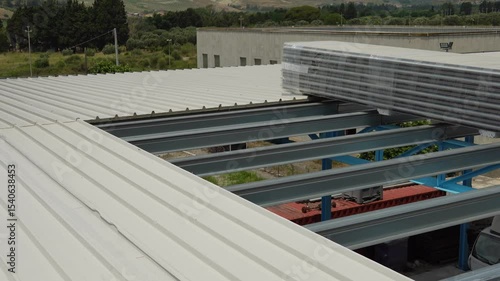 Sheet metal roofing on a steel structure under construction. Polyester sandwich panels. This image shows stacks of building materials on a metal roof of an industrial building.