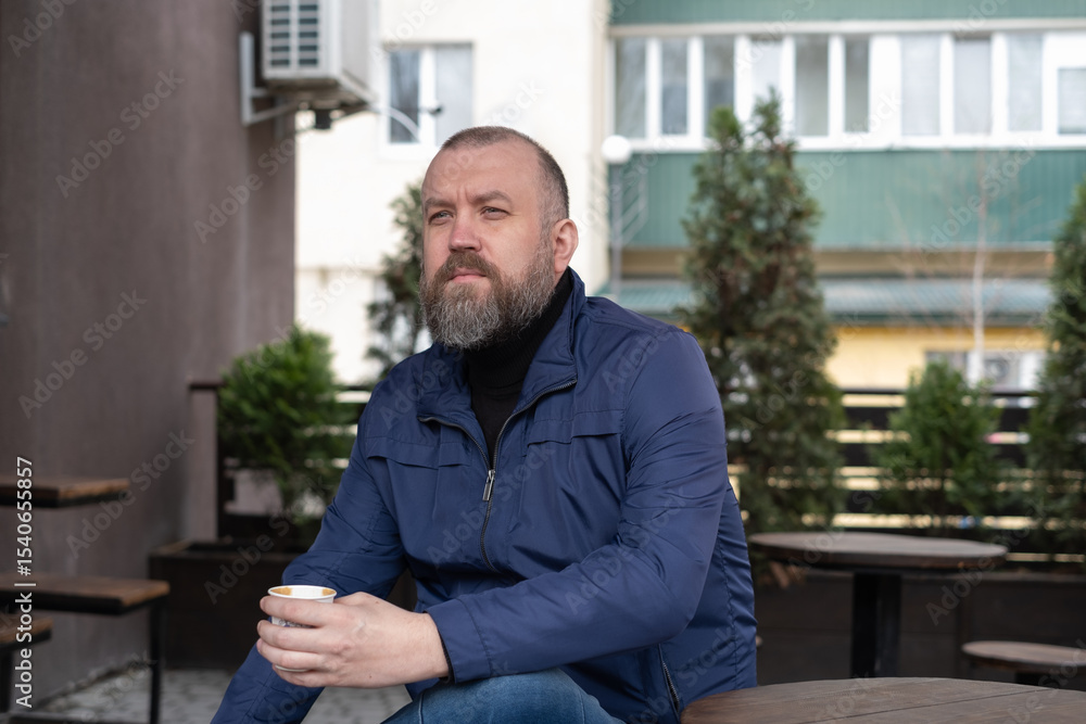 Obraz premium Man enjoying coffee while seated outdoors in a modern urban setting on a sunny day