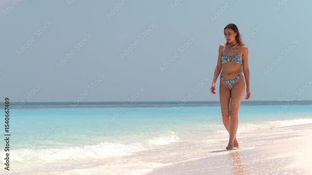 Young woman in bikini walking along the shoreline on tropical beach, smiling and enjoying summer breeze, clear sky and turquoise sea, vacation, travel and active lifestyle, happiness Young woman in bikini walking along the shoreline on tropical beach, smiling and enjoying summer breeze, clear sky and turquoise sea, vacation, travel and active lifestyle, happiness