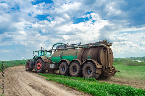 Tractor truck with manure driving through field. Large tractor with trailer of liquid manure. Side view. Dramatic sky.