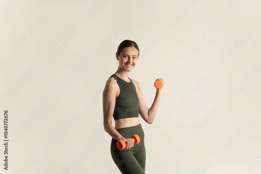 A girl in a green workout outfit enthusiastically holds an orange dumbbell in one hand and a tennis ball in the other, showcasing her fitness energy and readiness to exercise A girl in a green workout outfit enthusiastically holds an orange dumbbell in one hand and a tennis ball in the other, showcasing her fitness energy and readiness to exercise