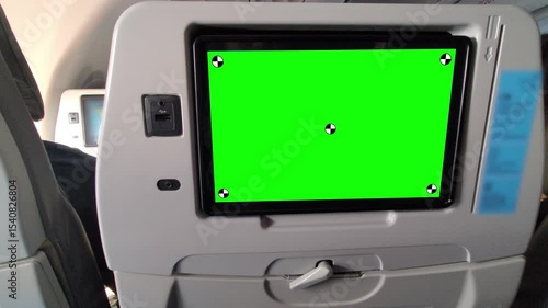 Close-up of an airplane seatback entertainment screen with green screen chroma key for video replacement, featuring a USB charging port, headphone jack, and seatback tray in a modern aircraft cabin