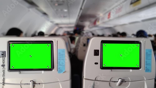 Interior view of a commercial airplane cabin with rows of passenger seats and seatback entertainment screens showing green screen placeholders, suitable for mockups or chroma key replacements