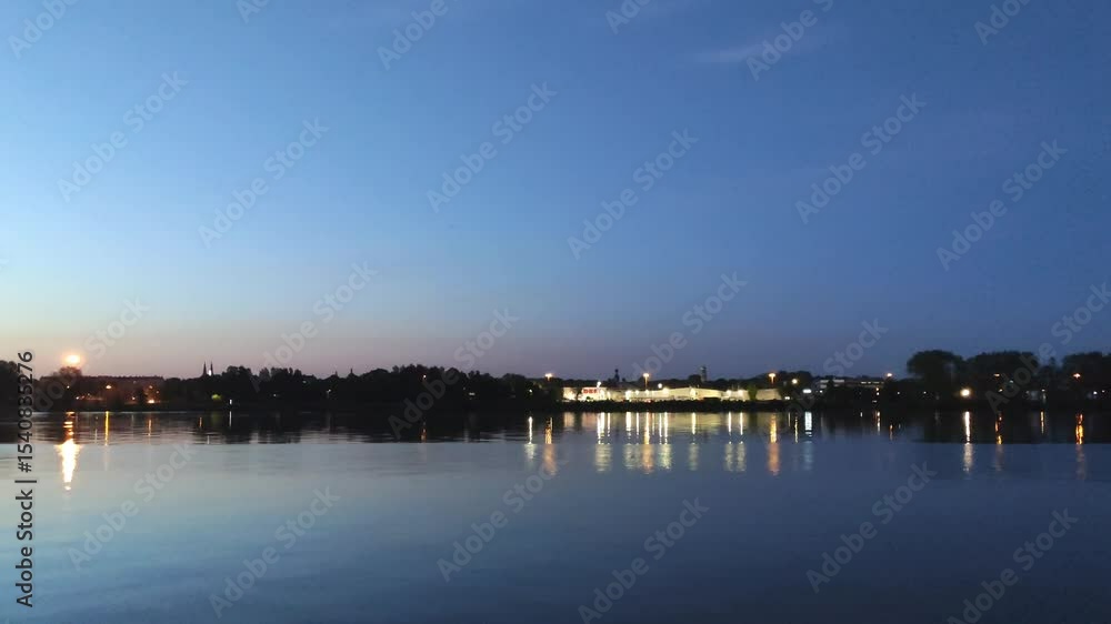 Nighttime cityscape reflected in calm river waters, featuring glowing lights, urban silhouettes, and mirror-like symmetry. A tranquil view. Nighttime cityscape reflected in calm river waters, featuring glowing lights, urban silhouettes, and mirror-like symmetry. A tranquil view.