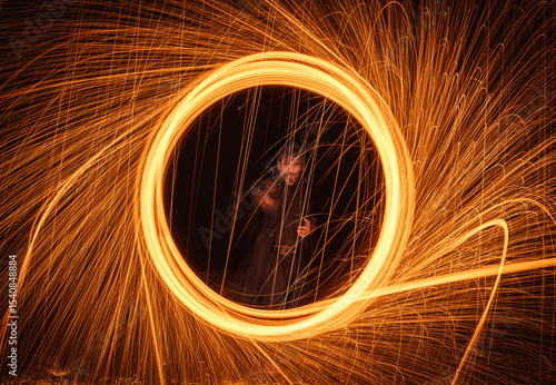 A witcher casting a magic spell in the form of a circle of fire that opens a portal and releases sparks, like in superhero films.