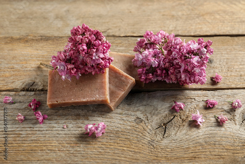 Soap bars and lilac flowers on wooden table, closeup