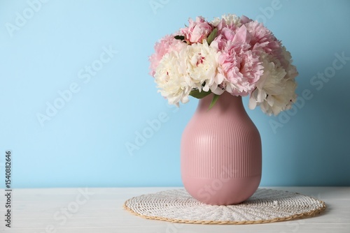 Fototapeta Naklejka Na Ścianę i Meble -  Beautiful peonies in vase on white table near light blue wall. Space for text
