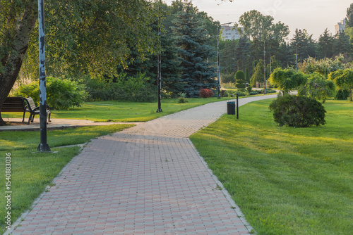 Fototapeta Naklejka Na Ścianę i Meble -  A beautiful summer green park with a brick pavement and walking path in the city