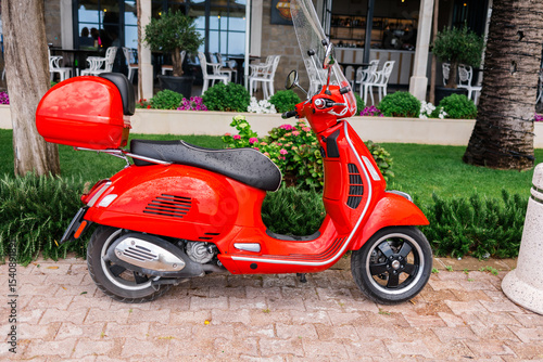 Red scooter parked on a city street near cafe. Urban mobility, personal transport, and summer commuting.