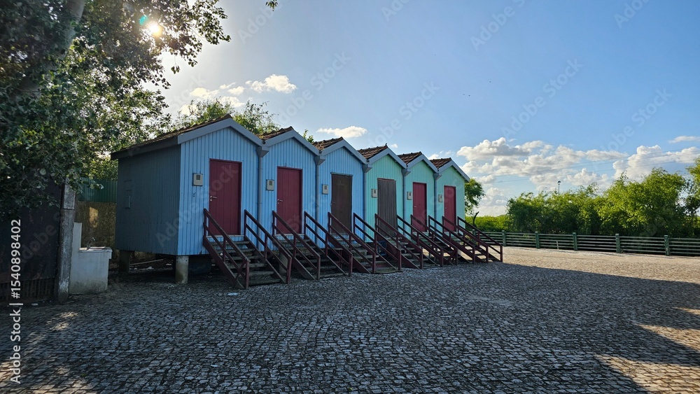 Naklejka premium Colorful Row of Elevated Wooden Huts with Trees – Scenic Rural View