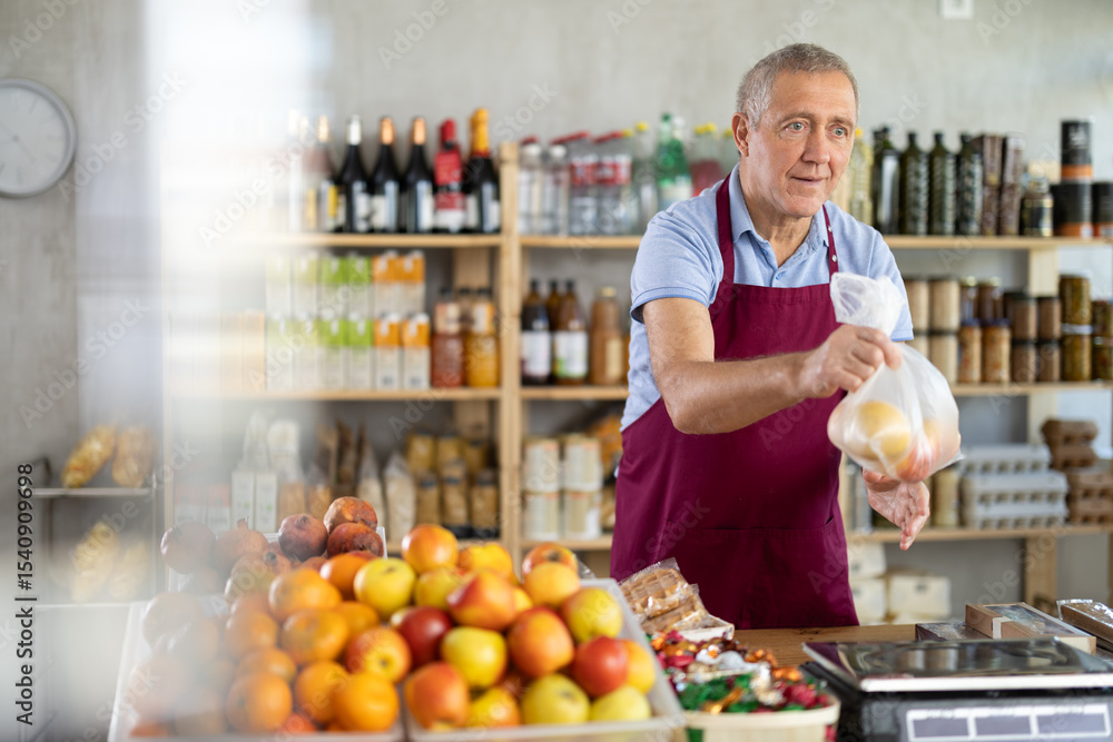 Polite mature male seller kindly giving apples in plastic bag in grocery store Polite mature male seller kindly giving apples in plastic bag in grocery store