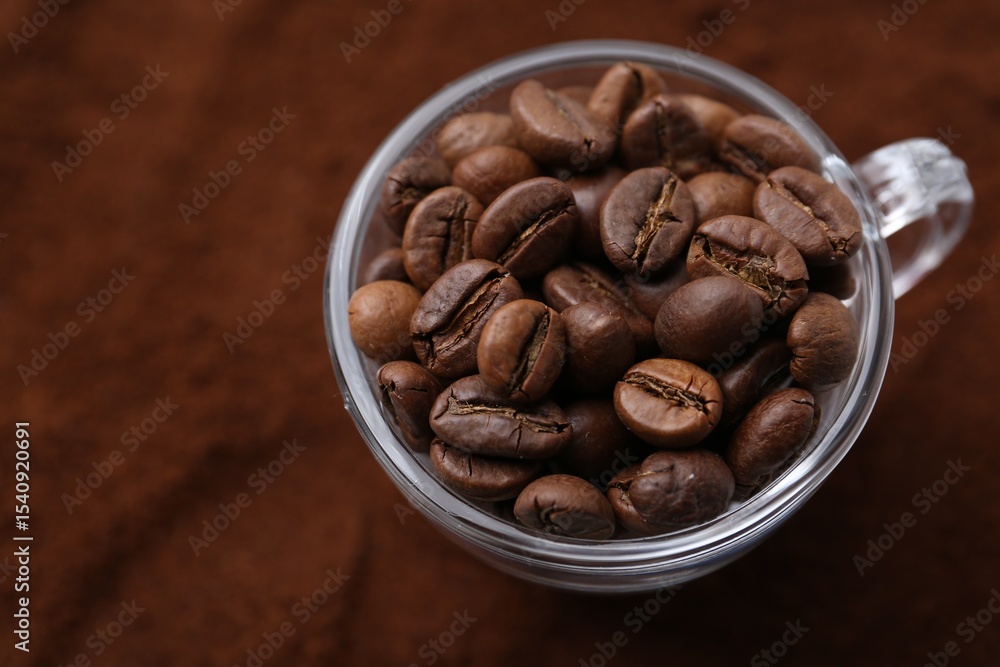 Fototapeta premium Cup of roasted coffee beans on powder, above view
