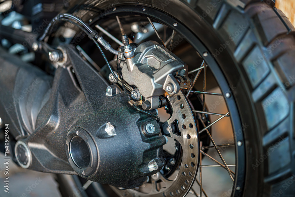 Detailed view of a motorcycle rear wheel showcasing braking system and tire tread design in a garage setting Detailed view of a motorcycle rear wheel showcasing braking system and tire tread design in a garage setting