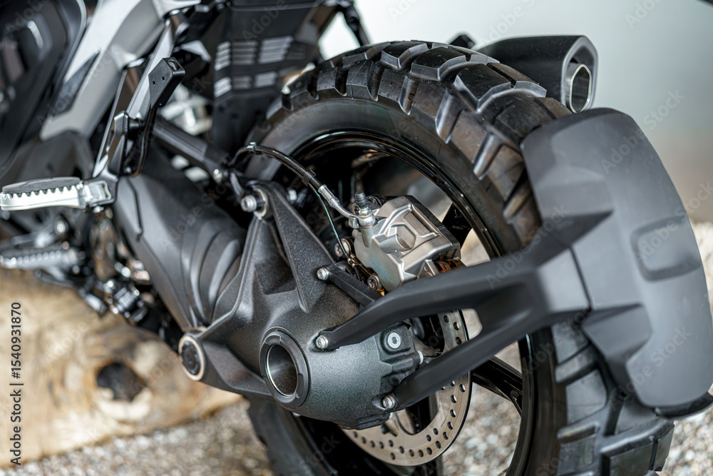 Obraz premium Close-up view of motorcycle rear wheel showing intricate details of braking and suspension components in urban setting