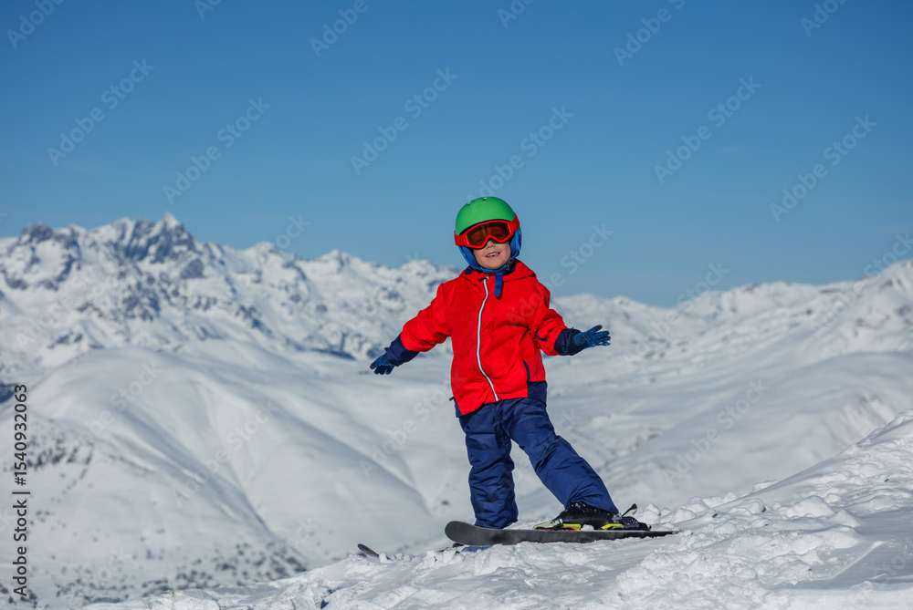 Child in red ski jacket turns while skiing atop a snowy ridge Child in red ski jacket turns while skiing atop a snowy ridge