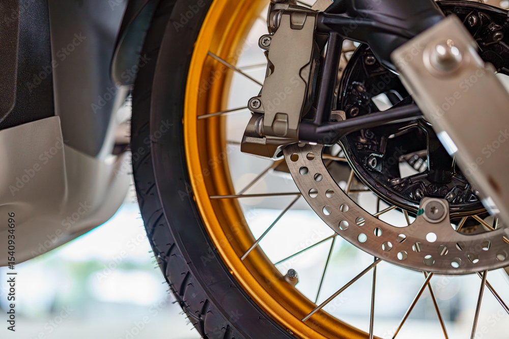 Fototapeta premium Motorcycle wheel with golden rim and brake system captured in bright garage setting during maintenance
