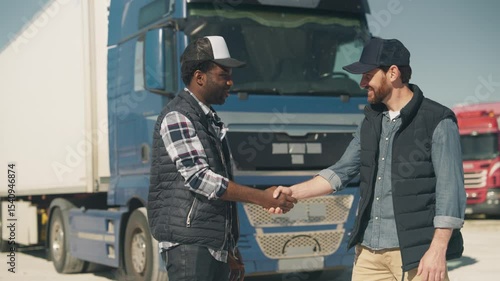 Two cheerful men shaking hands in bright daylight while standing in front of massive truck. Smiling and building trust. Finalizing agreement or celebrating smooth coordination on site.