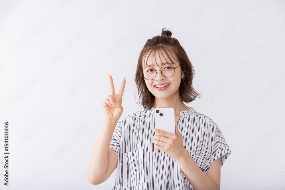 Obraz premium スマートフォン片手にブイサインをする女子大生