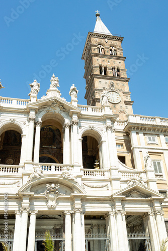 A front view of the Papal Basilica of Santa Maria Maggiore and its clock, from Piazza Santa Maria Maggiore, on a sunny day.